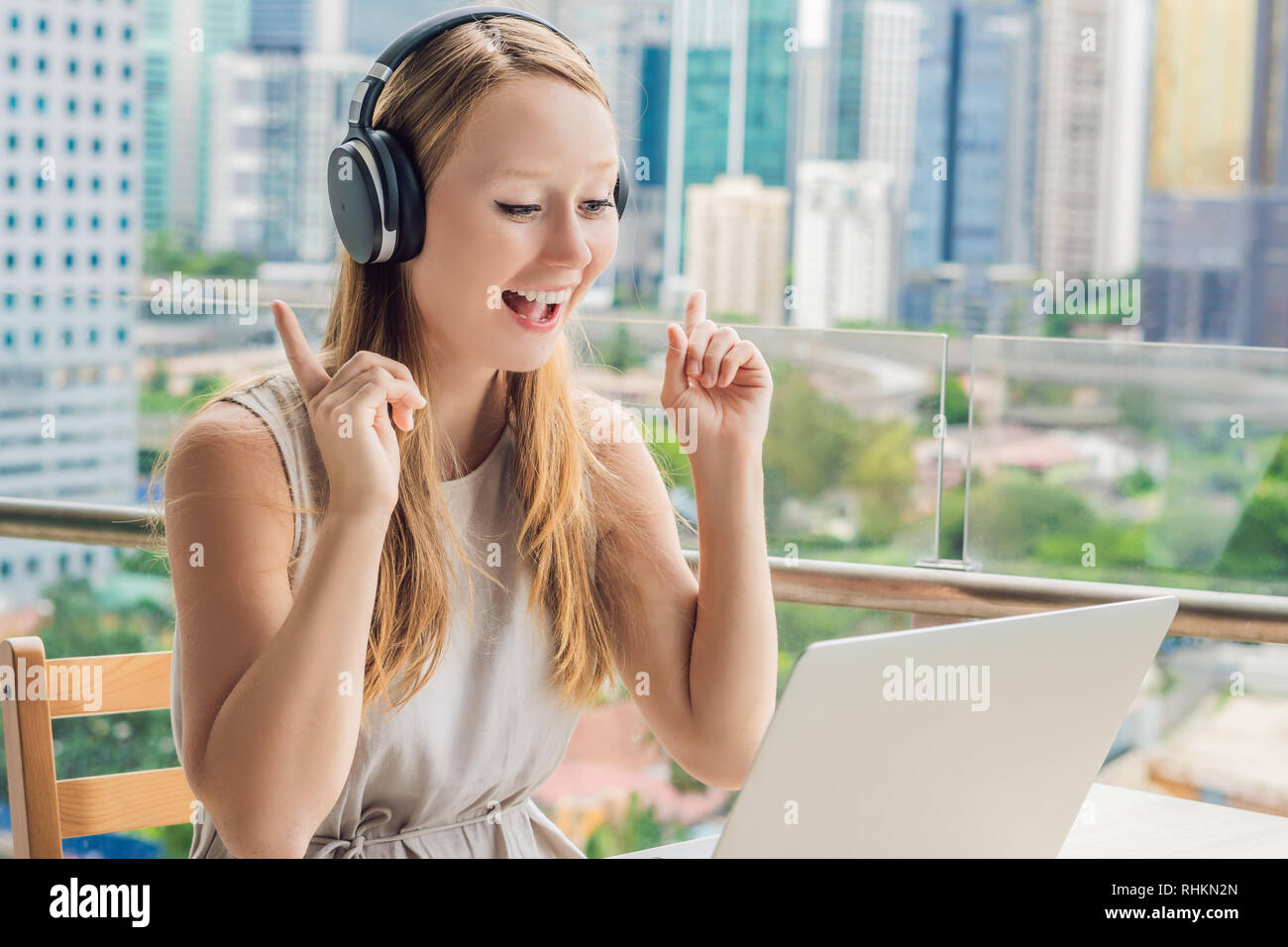 Junge Frau lehrt eine Fremdsprache lernt eine Fremdsprache im Internet auf ihrem Balkon vor dem Hintergrund einer großen Stadt. Online Sprache Stockfoto