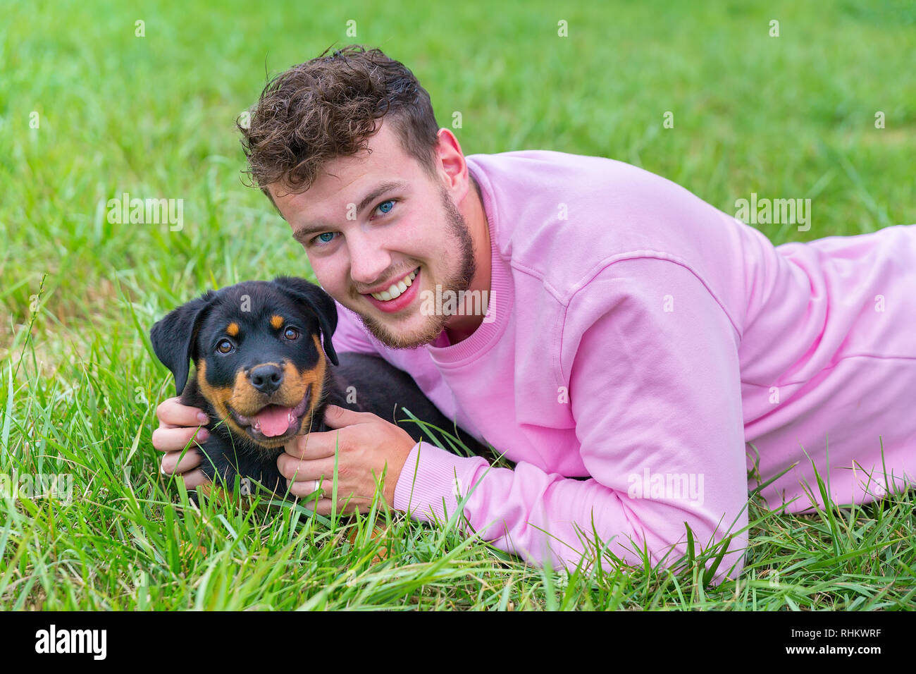 Junge kaukasier männlich Hundebesitzer hält liebevoll Rottweiler Welpen in natürlichen Wiese Stockfoto