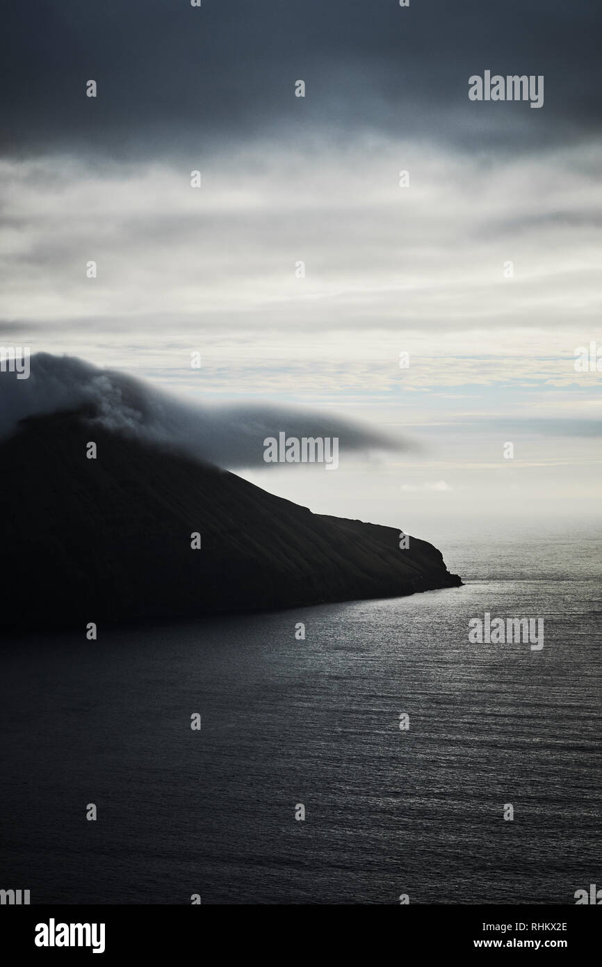 Koltur Insel und Wolken - Eine minimal launische Landschaft der Färöer Inseln im Nordatlantik - dunkle Inselseeseite Stockfoto