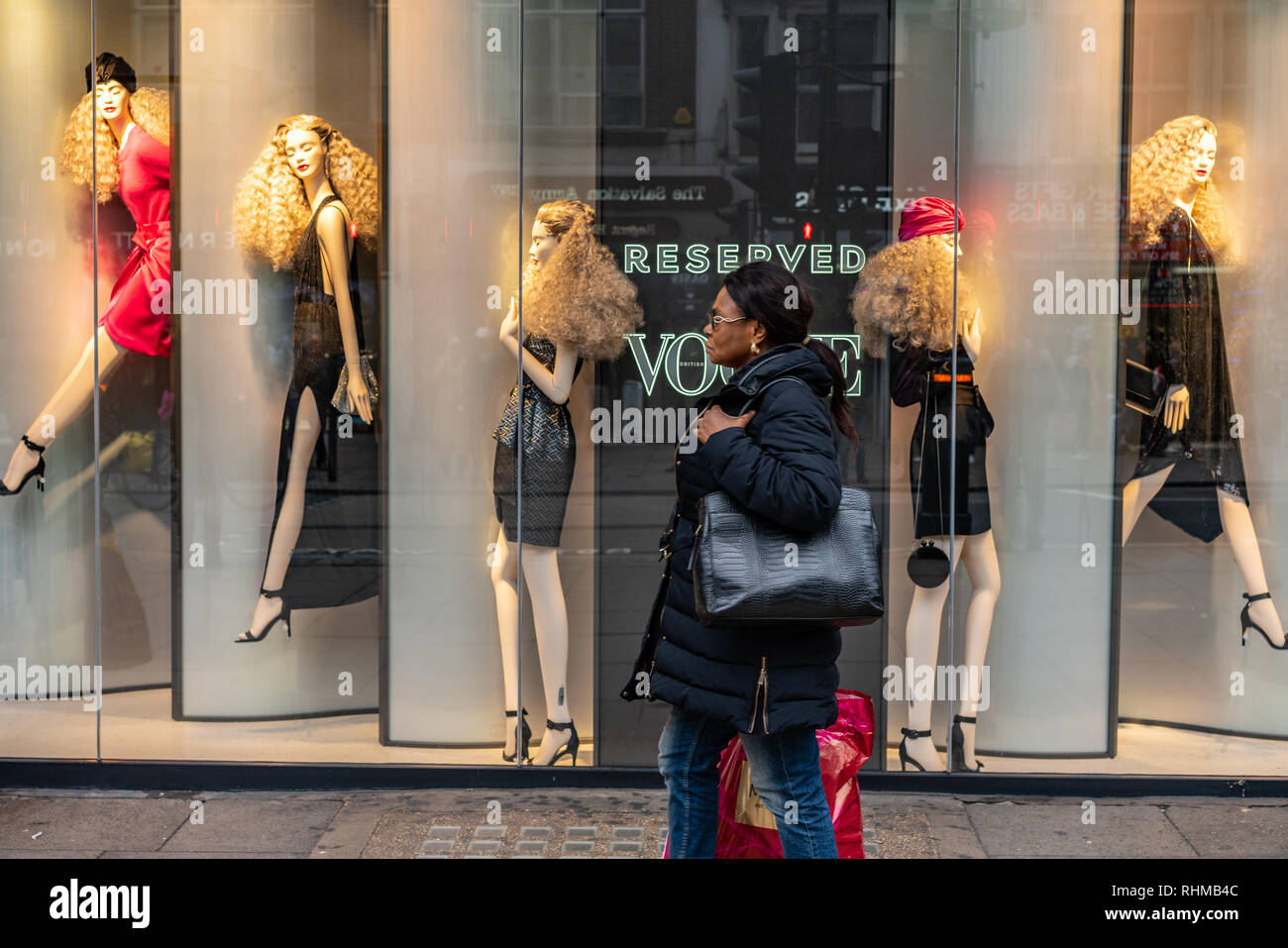 Eine schwarze Dame macht ihren Weg hinter einem Shop vorne an der Londoner Oxford Street. Die schaufensterpuppen im Fenster sind alle Weiß/Kaukasisch Darstellung Stockfoto