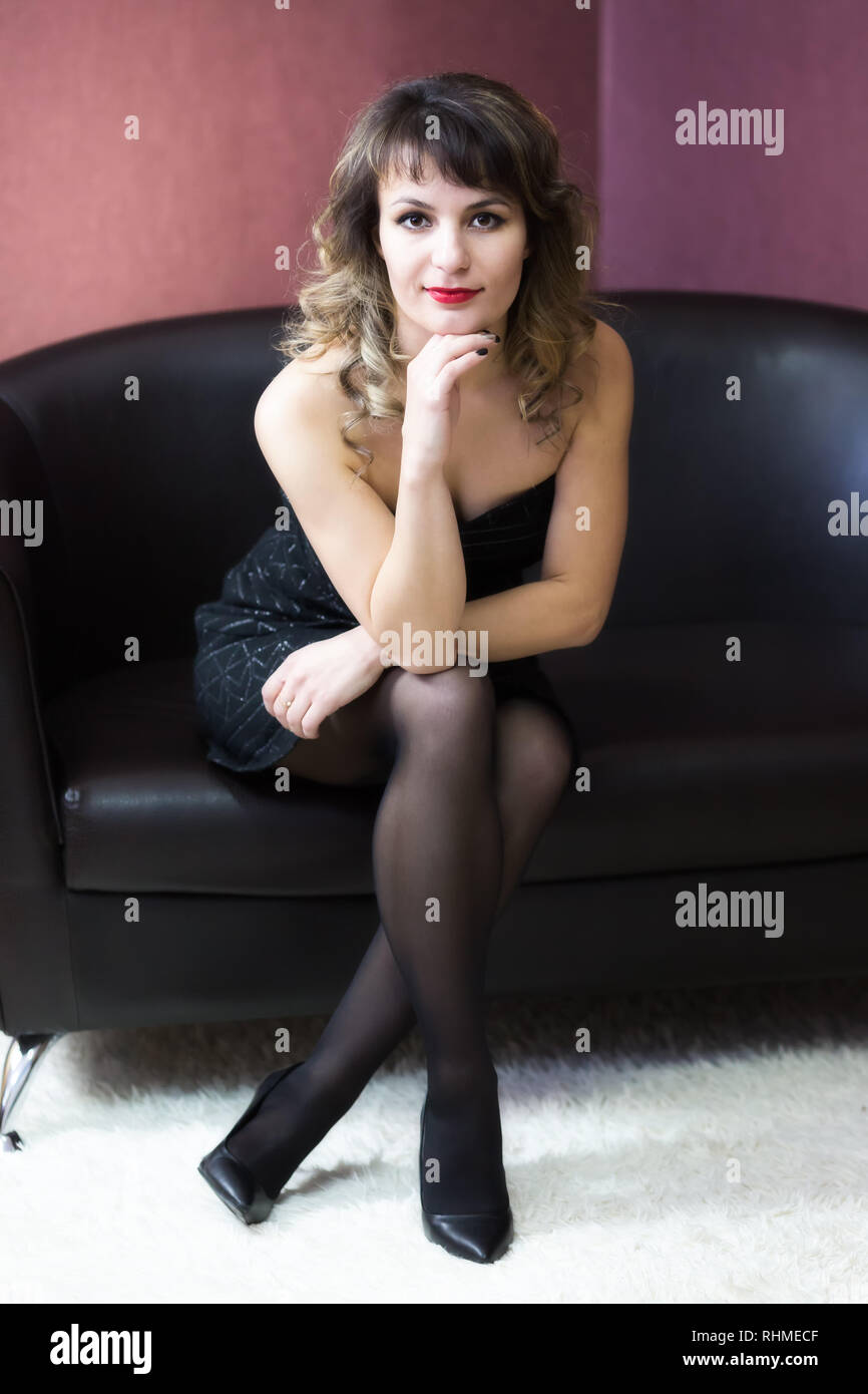 Ein Mädchen in einem kurzen schwarzen Kleid saß auf dem Sofa. Stockfoto