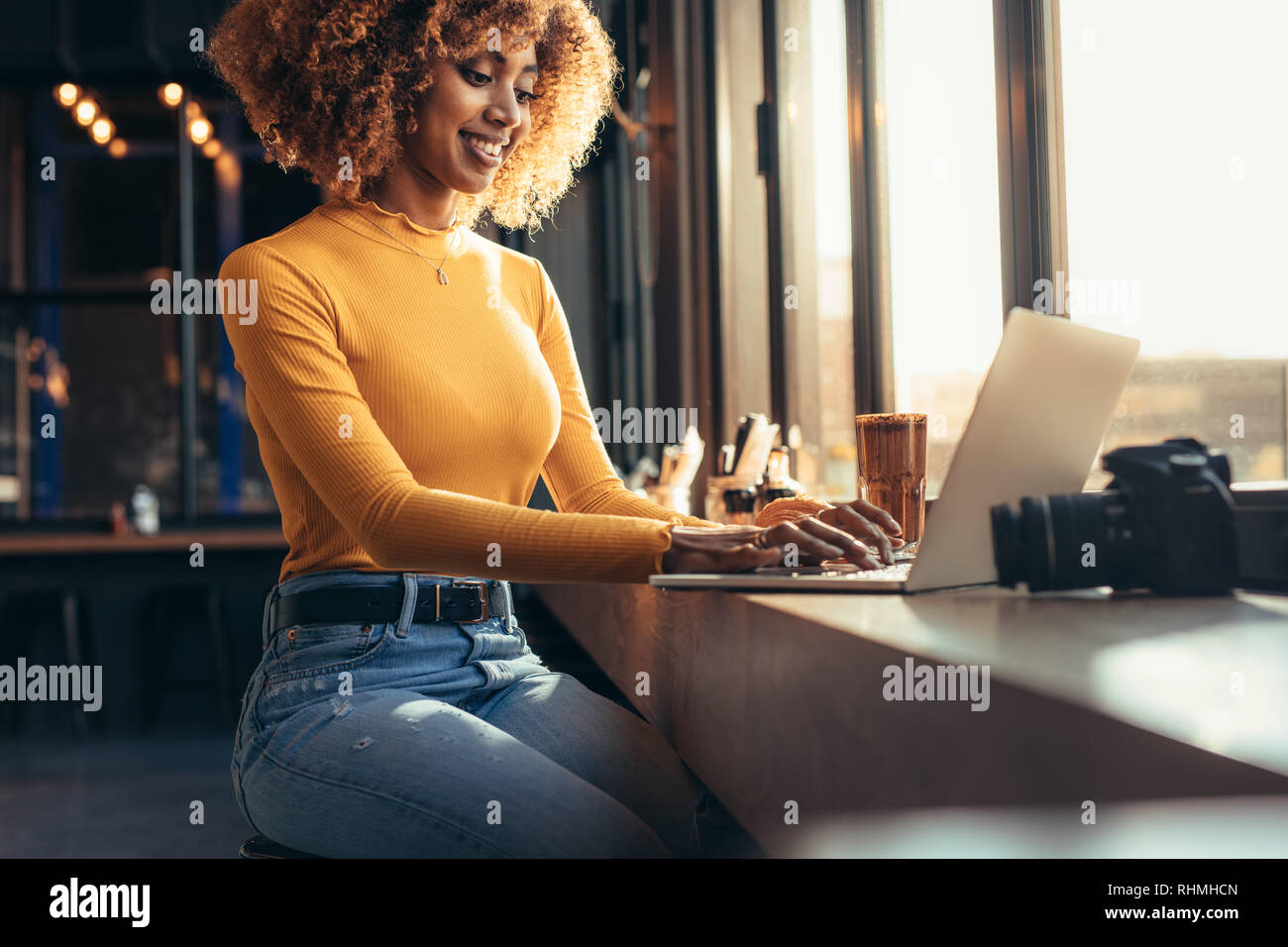 Freier Fotograf sitzt in einem Restaurant in der Nähe eines Fensters Arbeiten am Laptop. Lächelnd afro-amerikanische Blogger Arbeiten am Laptop mit einem Digita Stockfoto