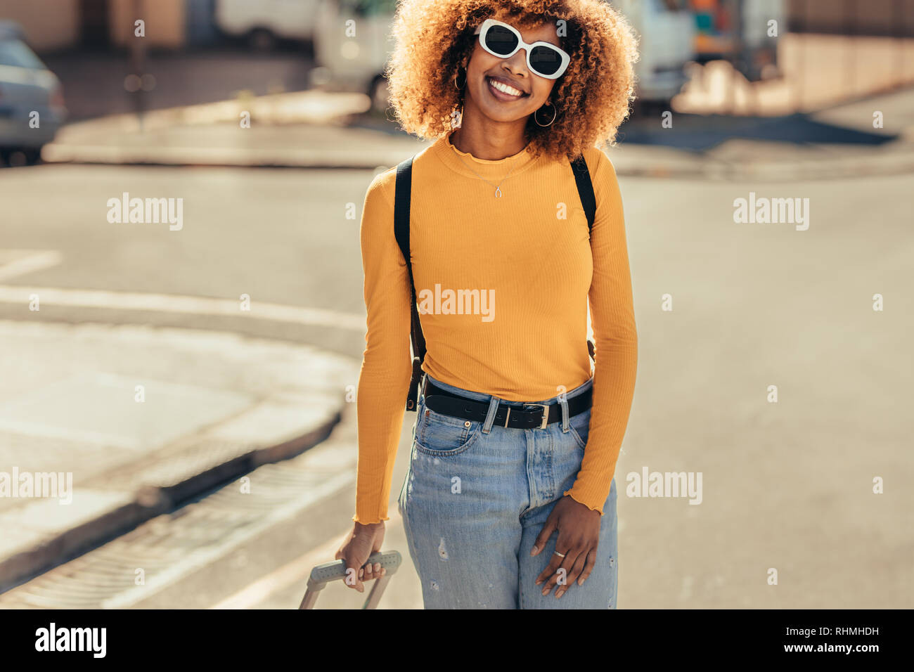 Weibliche afro-amerikanische Reisende im Urlaub um die Stadt zu Fuß zu erkunden. Lächelnde Frau mit Sonnenbrille und einen Rucksack zu Fuß auf die Straße. Stockfoto