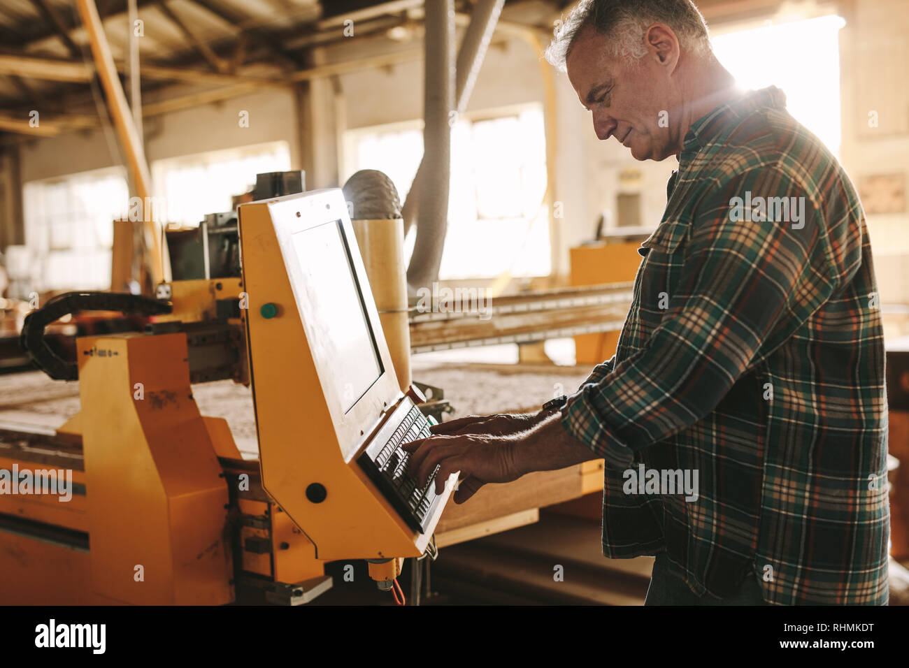 Ältere männliche Tischler Programmierung einer CNC-Holzbearbeitung Maschine in der Werkstatt. Reifer Mann bereitet ein Programm für die CNC-Maschine bei Schreinerei Stockfoto