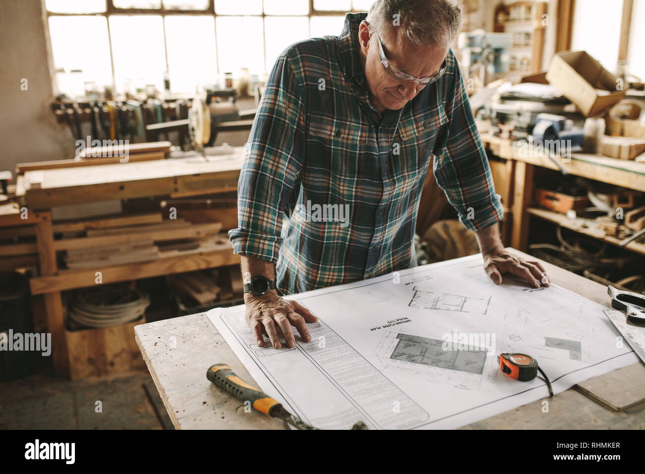 Senior carpenter Lesung Zeichnung in der Werkstatt Bank. Reife Männer studieren Gebäude Grundriss vor Beginn der Arbeiten in der Schreinerei. Stockfoto