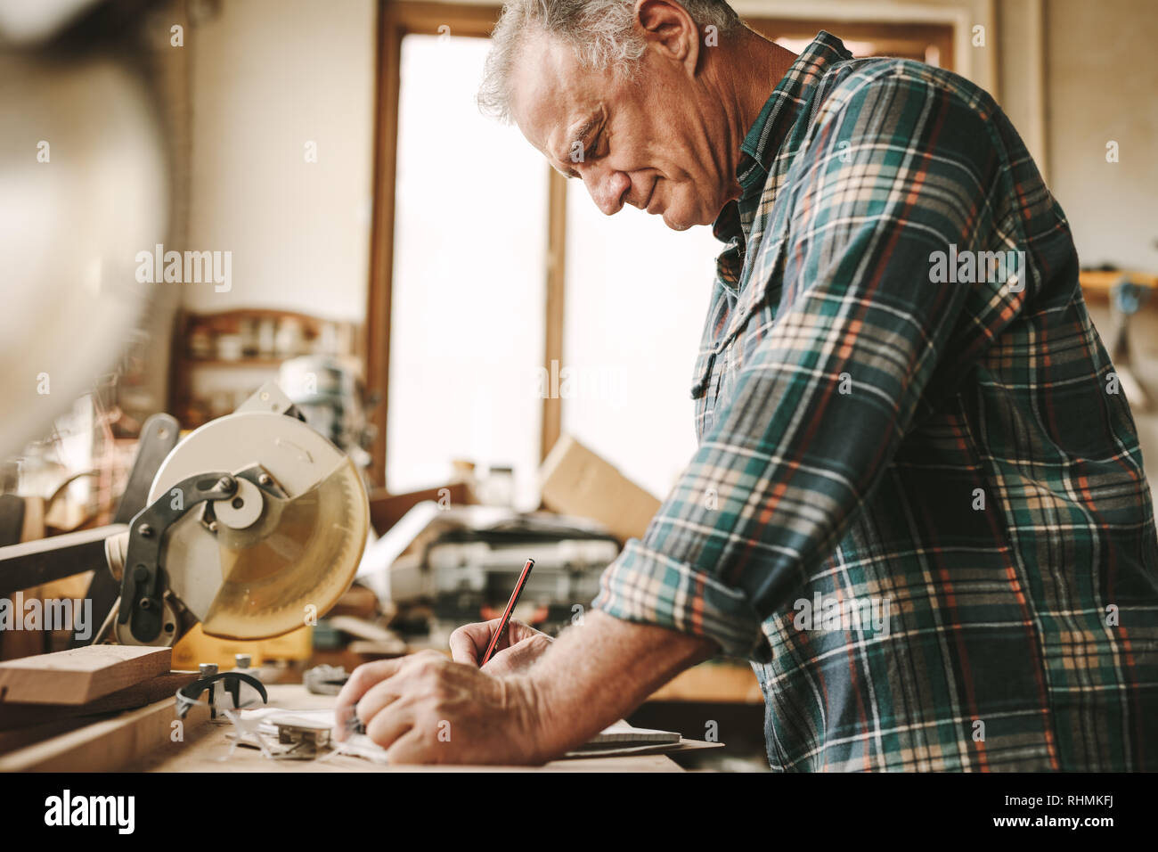 Senior Zimmermann Notizen in seinem Buch in der Werkstatt. Reife männliche Tischler seine Arbeit Planung Zimmerei. Stockfoto