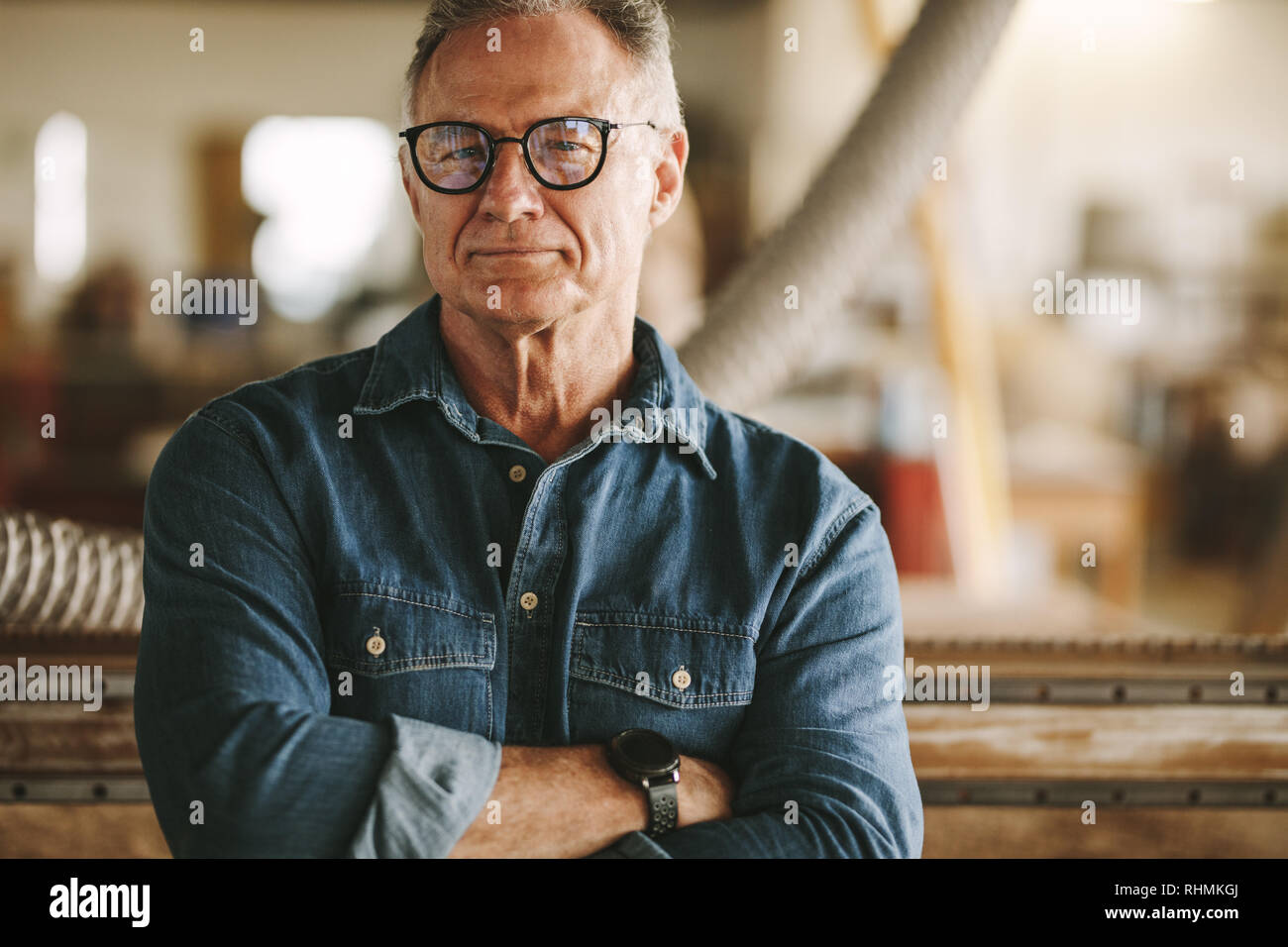 Portrait von erfolgreichen älteren Mann in Brillen stehen in seiner Schreinerei. Stolz Schreinerei Inhaber Stehen mit verschränkten Armen. Stockfoto