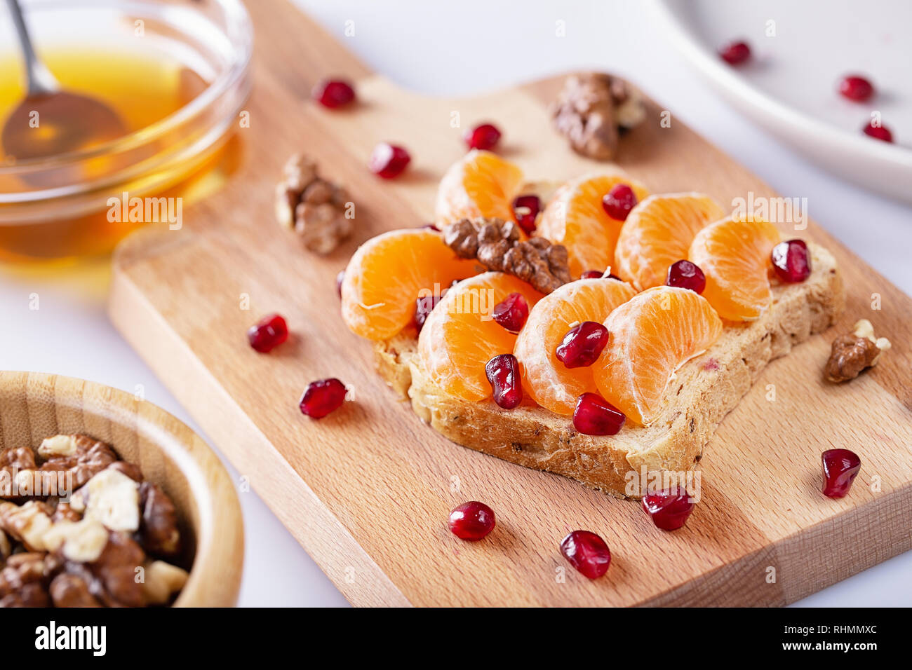Sandwich mit Granatapfel Getreide, Honig, Nüsse und Mandarinen auf weißen Hintergrund. Roh essen. Gesunde Lebensmittel für Frühstück oder Mittagessen. Selektive konzentrieren. Stockfoto