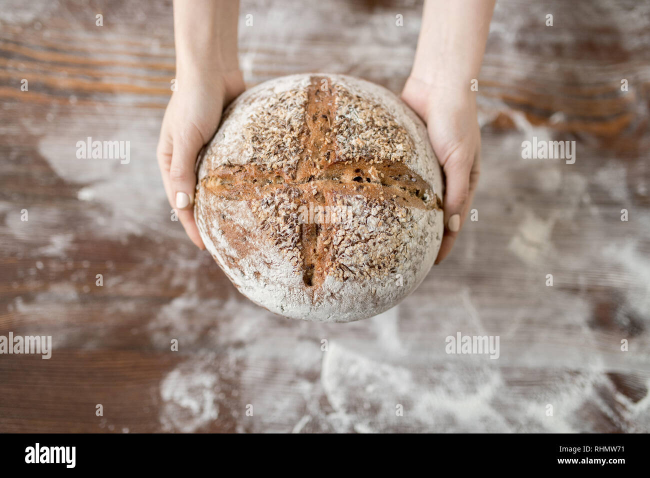 Überblick über frische Roggen homememade runde Brot durch weibliche Hände über Tisch und Mehl statt Stockfoto