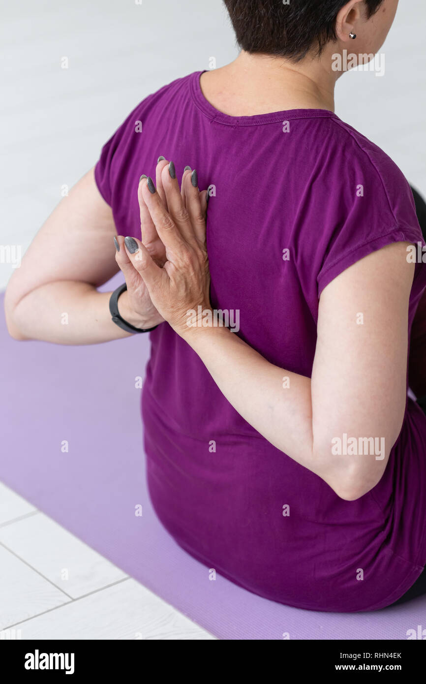 Leute, Sport, Yoga und Gesundheit Konzept - Mitte - gealterte Frau sitzt auf der Yogamatte mit Hände hinter dem Rücken Nahaufnahme Stockfoto