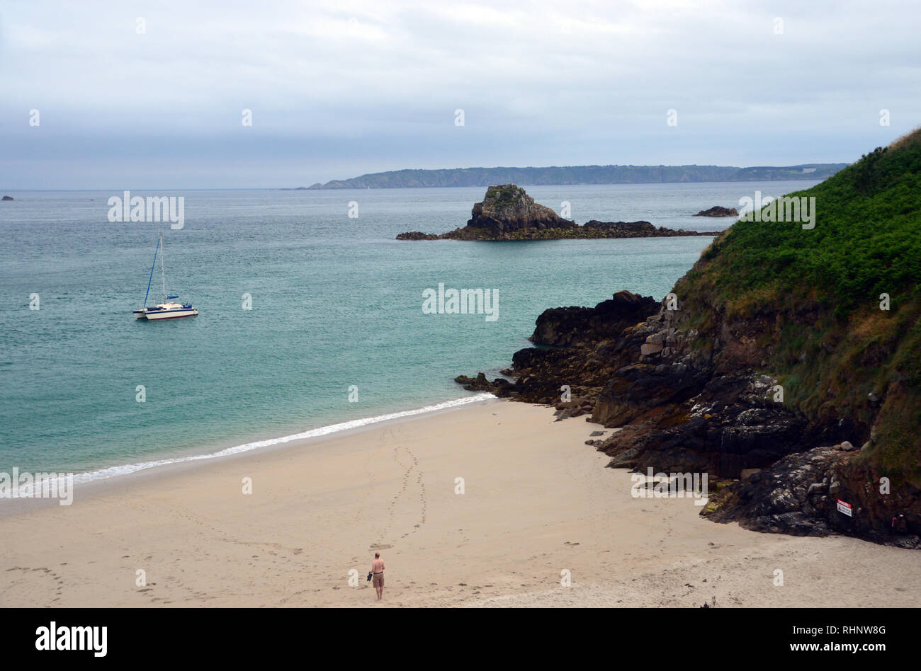 Mann an Segelboot Günstig in Belvoir Strand Blick von der Küste weg auf die Insel Herm, Channel Islands.de. Stockfoto