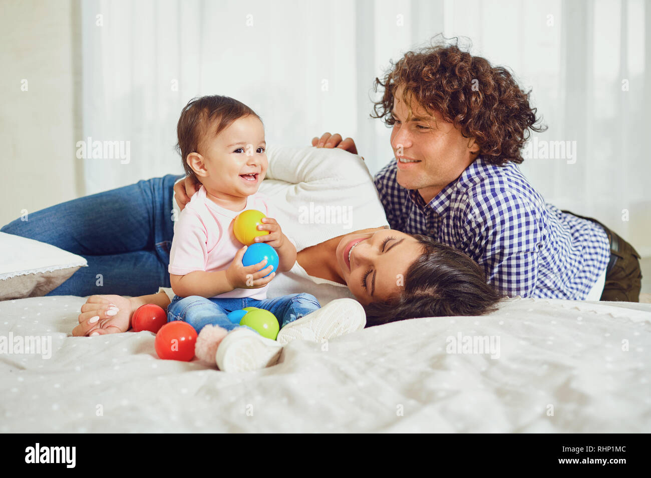 Happy Family spielen mit dem Baby im Zimmer. Junge Mutter und Vater spielen mit der Tochter auf einem Bett drinnen. Stockfoto