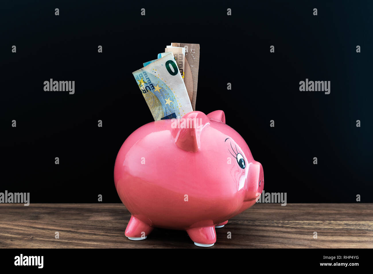 Bargeld in Sparschwein auf schwarzem Hintergrund Stockfoto