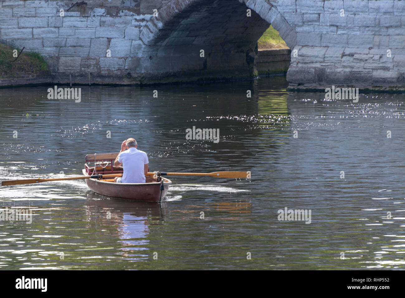 Mann im Ruderboot Kratzer Kopf mit alte steinerne Brücke arch im Hintergrund Stockfoto