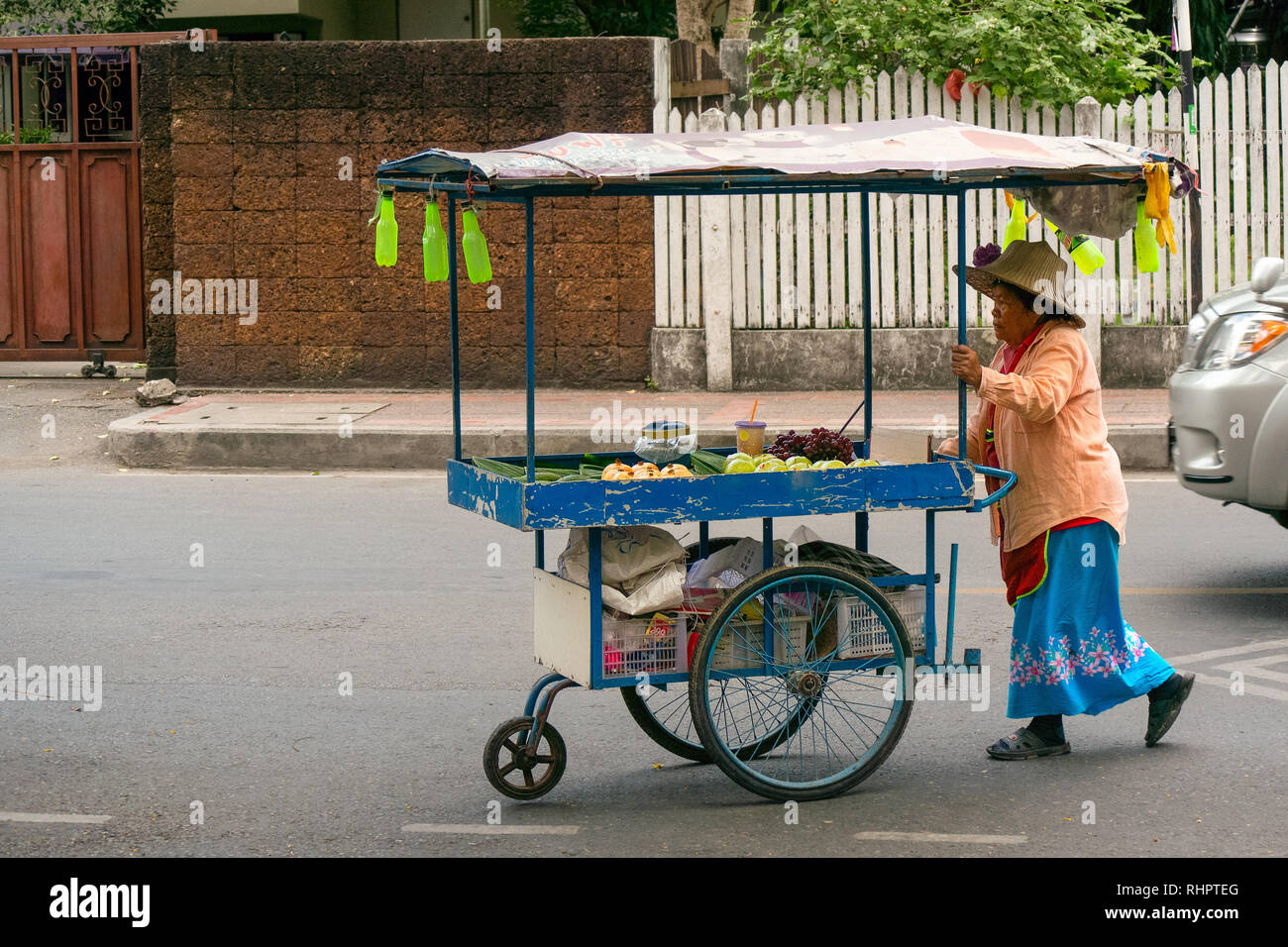 Eine alte asiatische Frau schiebt ihr die Frucht Wagen durch die Straßen von Chiang Mai, Thailand. Stockfoto