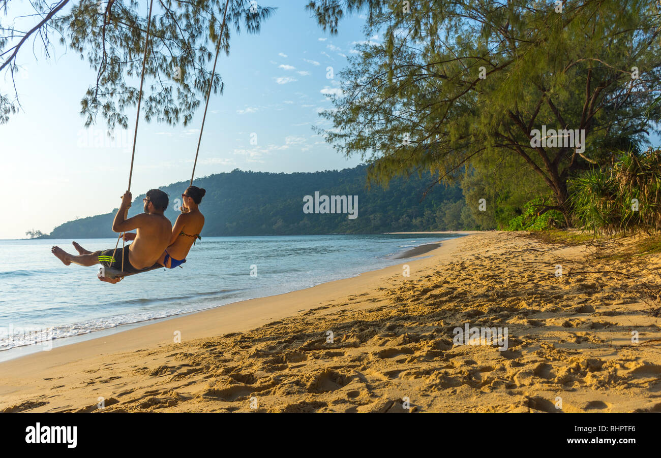 Ein junges Paar in Beach wear Schwingen auf einem Basic swing Über einem goldenen Sandstrand in paradiesischer Lage. Stockfoto