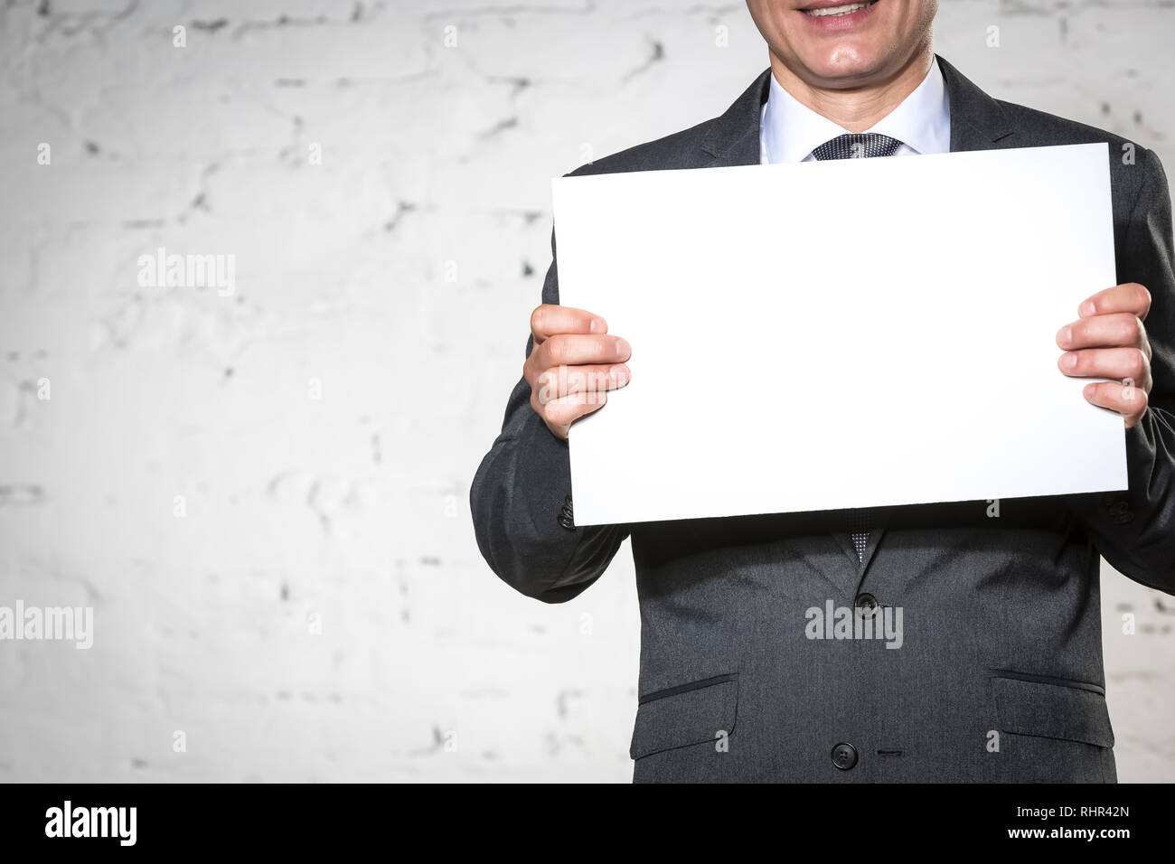 Mittelteil der lächelnden Geschäftsmann Holding leeres Plakat während gegen weiße Mauer stehend Stockfoto