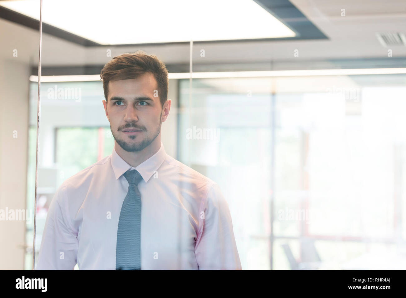 Nachdenkliche junge Professionelle durch Glas Fenster im Büro suchen Stockfoto