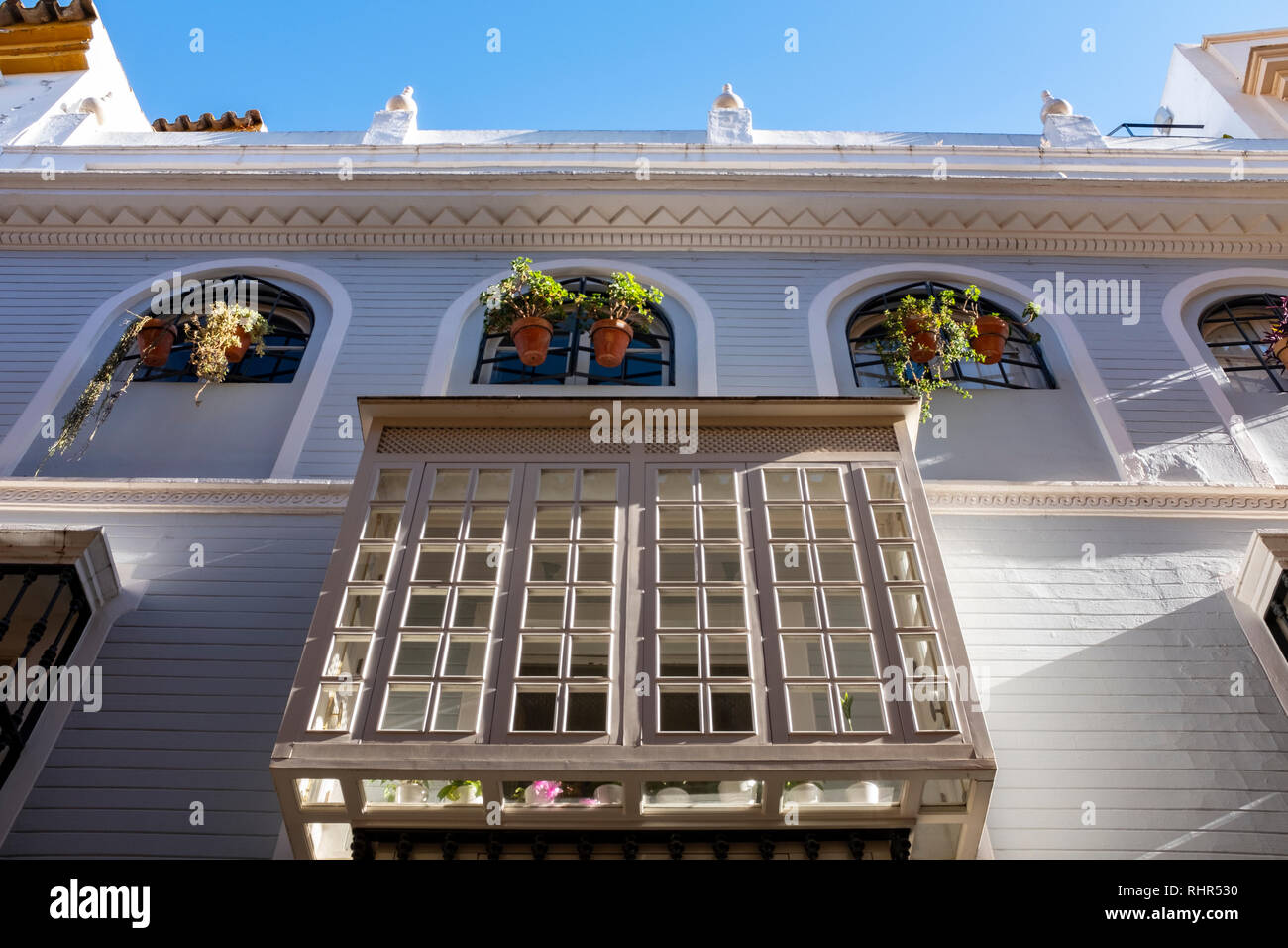 Schöne boxed Glas Balkon auf Pastell grau gefärbte shiplap Holz verkleideten Haus im Sonnenlicht mit Blumenkästen und Pflanzen Sevilla Spanien gebadet Stockfoto
