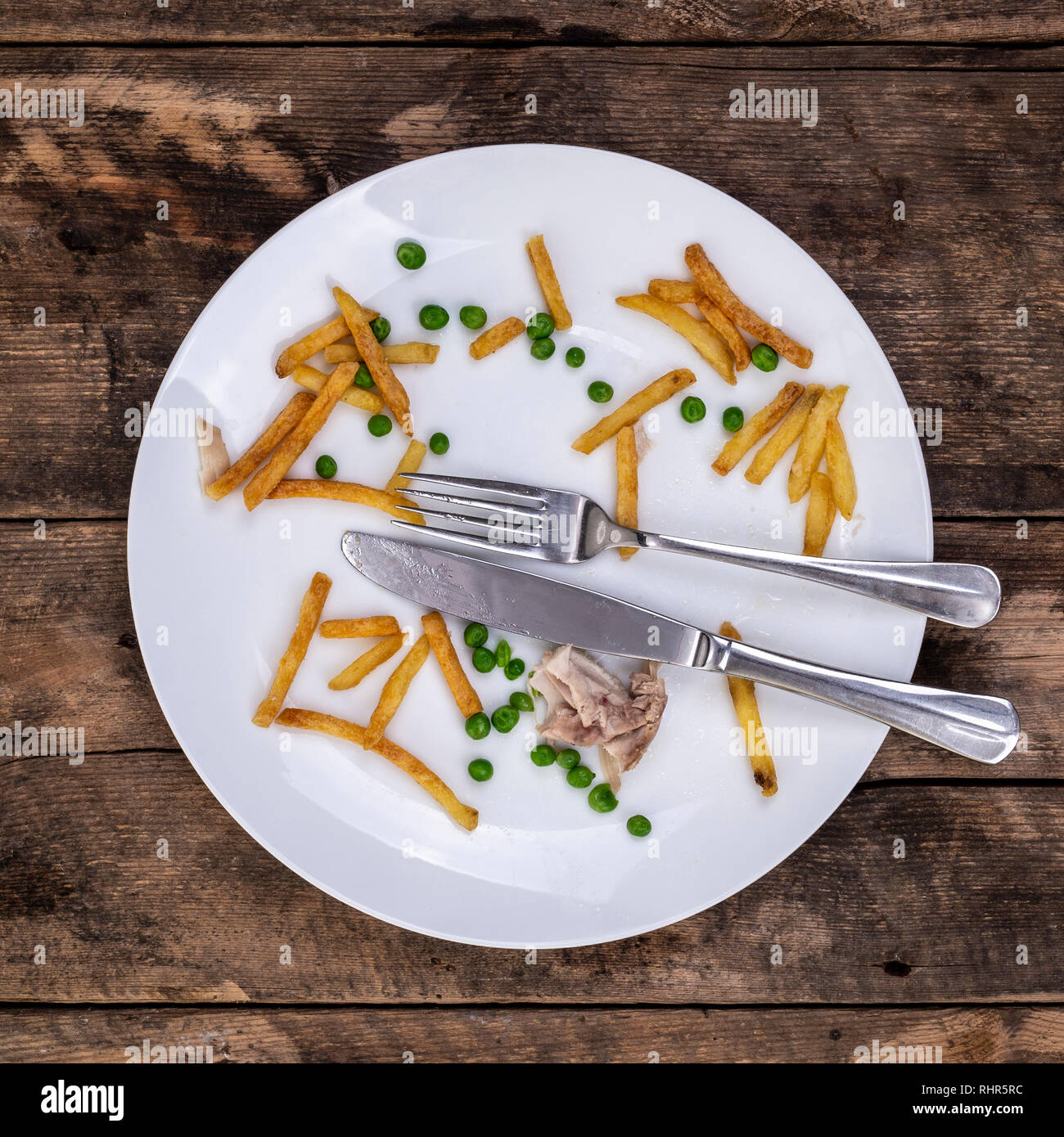 Reste von Chips Erbsen und Huhn auf einem mit Teller mit Messer und Gabel in einem rustikalen Holzmöbeln Hintergrund Stockfoto