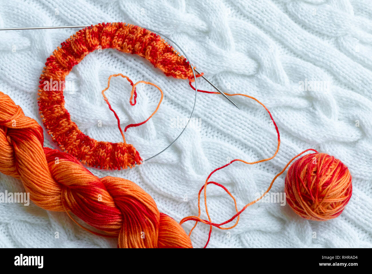 Stricken Projekt in Bearbeitung. Ein Stück stricken mit einer Kugel und einem Strang der rot-orange Farbe der Schnitt färben und Stricken auf dem Hintergrund einer Stockfoto