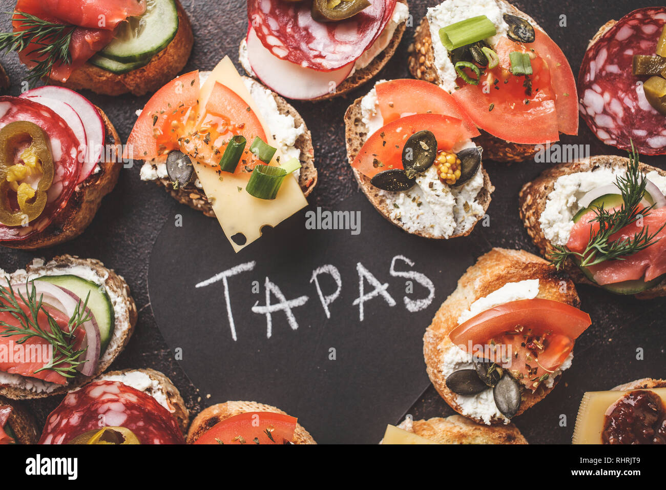 Verschiedene spanische Tapas mit Fisch, Wurst, Käse und Gemüse. Dunkler Hintergrund, flach. Stockfoto
