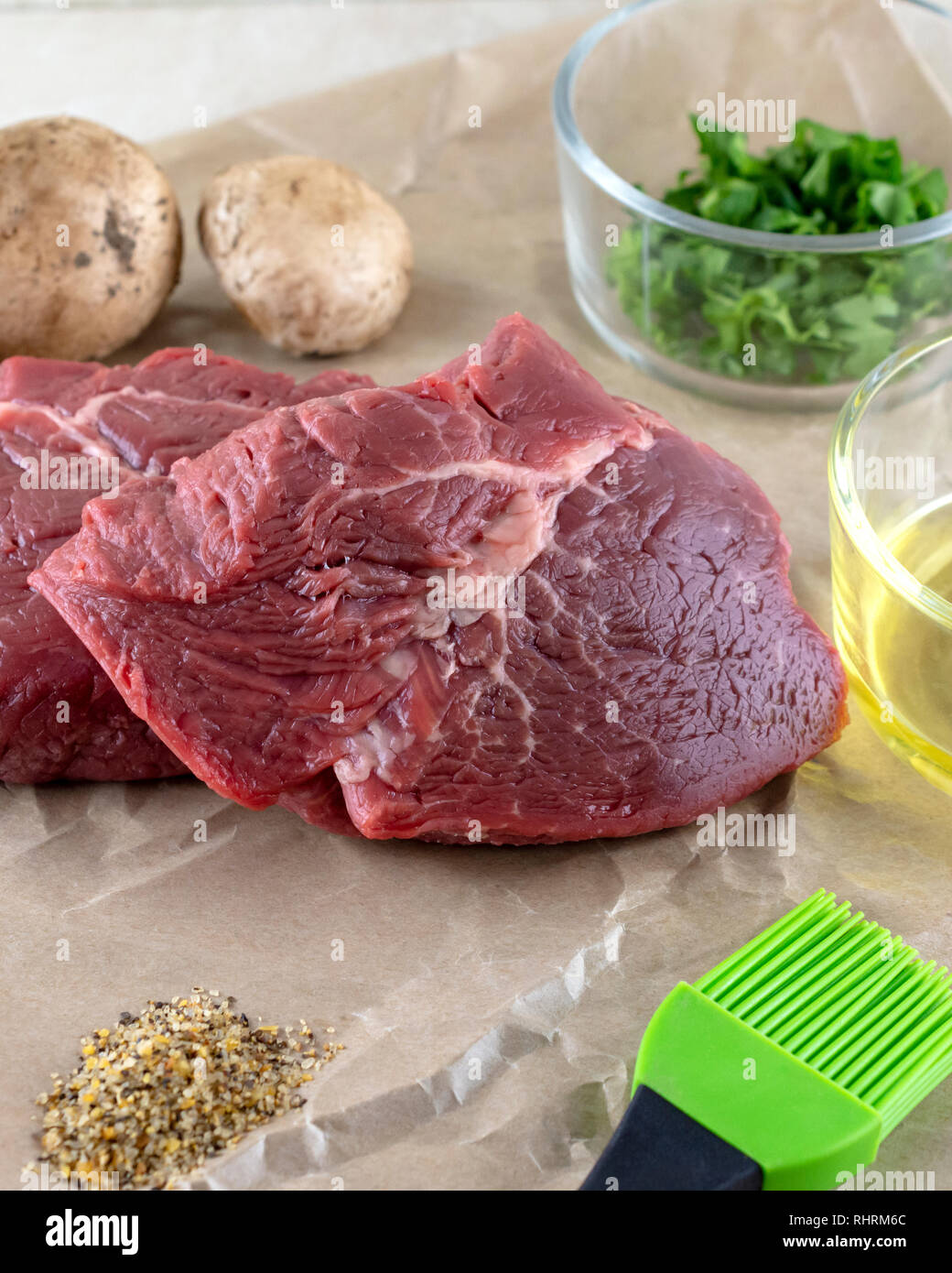 Zwei Steaks vorbereitet für das Kochen. Öl- und verschiedenen Gewürzen und Kräutern. Pilze im Hintergrund. Stockfoto