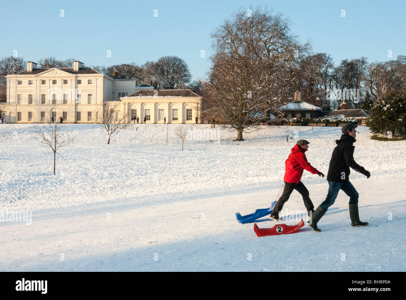 An einem klaren schneereichen Wintern Tag ein paar junge Männer gehen zügig und mit ihren Schlitten vor Kenwood House, London, UK. Stockfoto