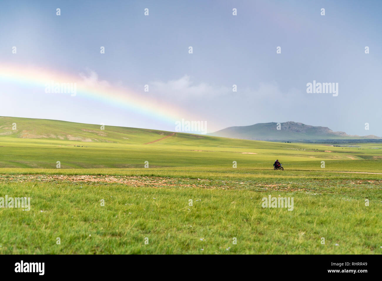 Mann, sein Motorrad und Regenbogen über dem grünen Mongolische Steppe. Ovorkhangai Provinz der Mongolei. Stockfoto