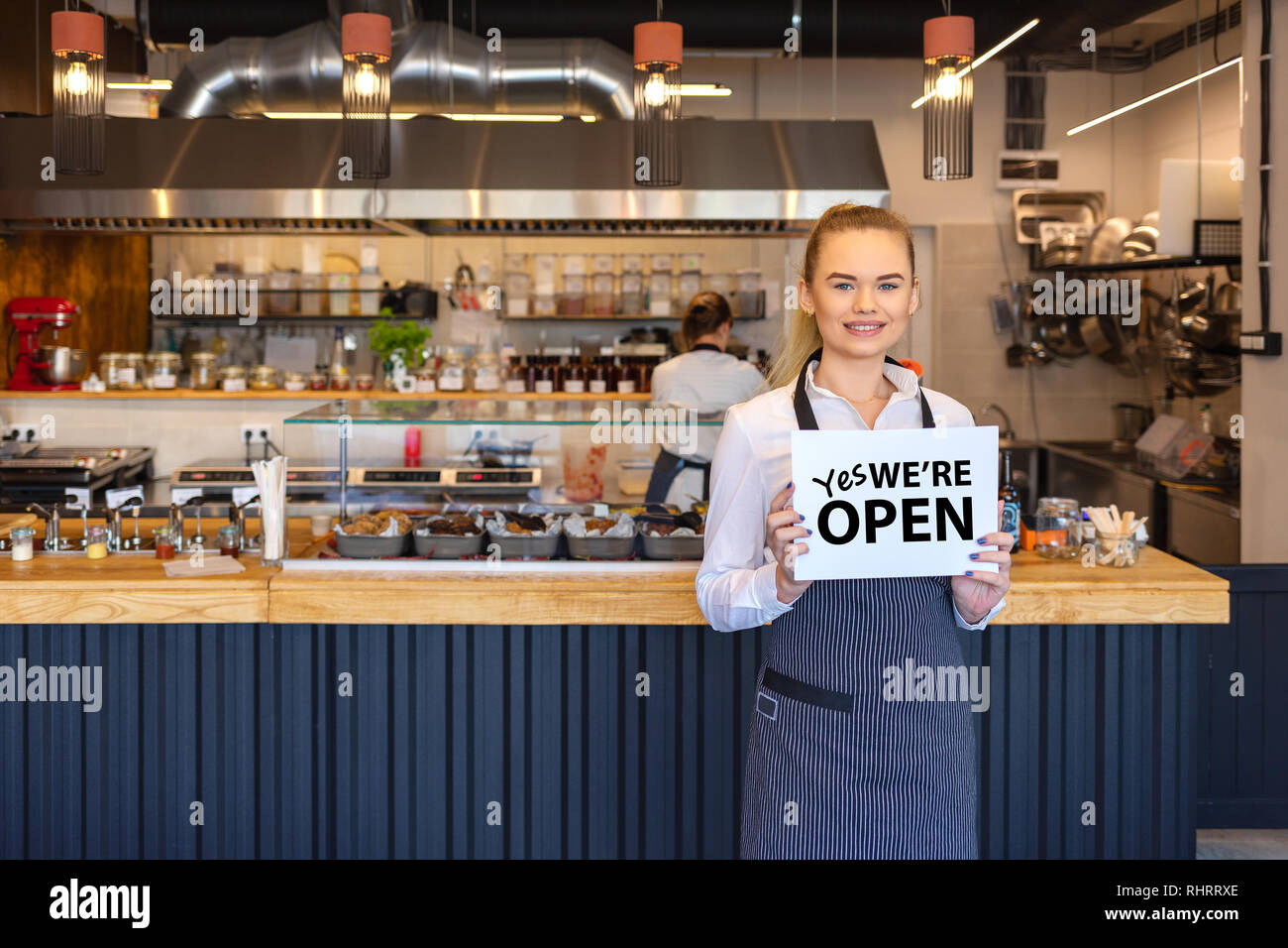 Portrait von lächelnden Eigentümer steht in seinem Restaurant mit offenem Namensschild. Junge Unternehmer Frau an Small Business Family Restaurant Stockfoto