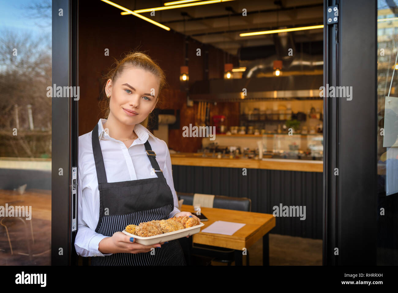 Portrait von lächelnden Eigentümer stehen im Restaurant Tür Holding gebackene Hackfleischbällchen. Junge Unternehmer Frau an kleinen Familienbetrieb Restaurant Stockfoto