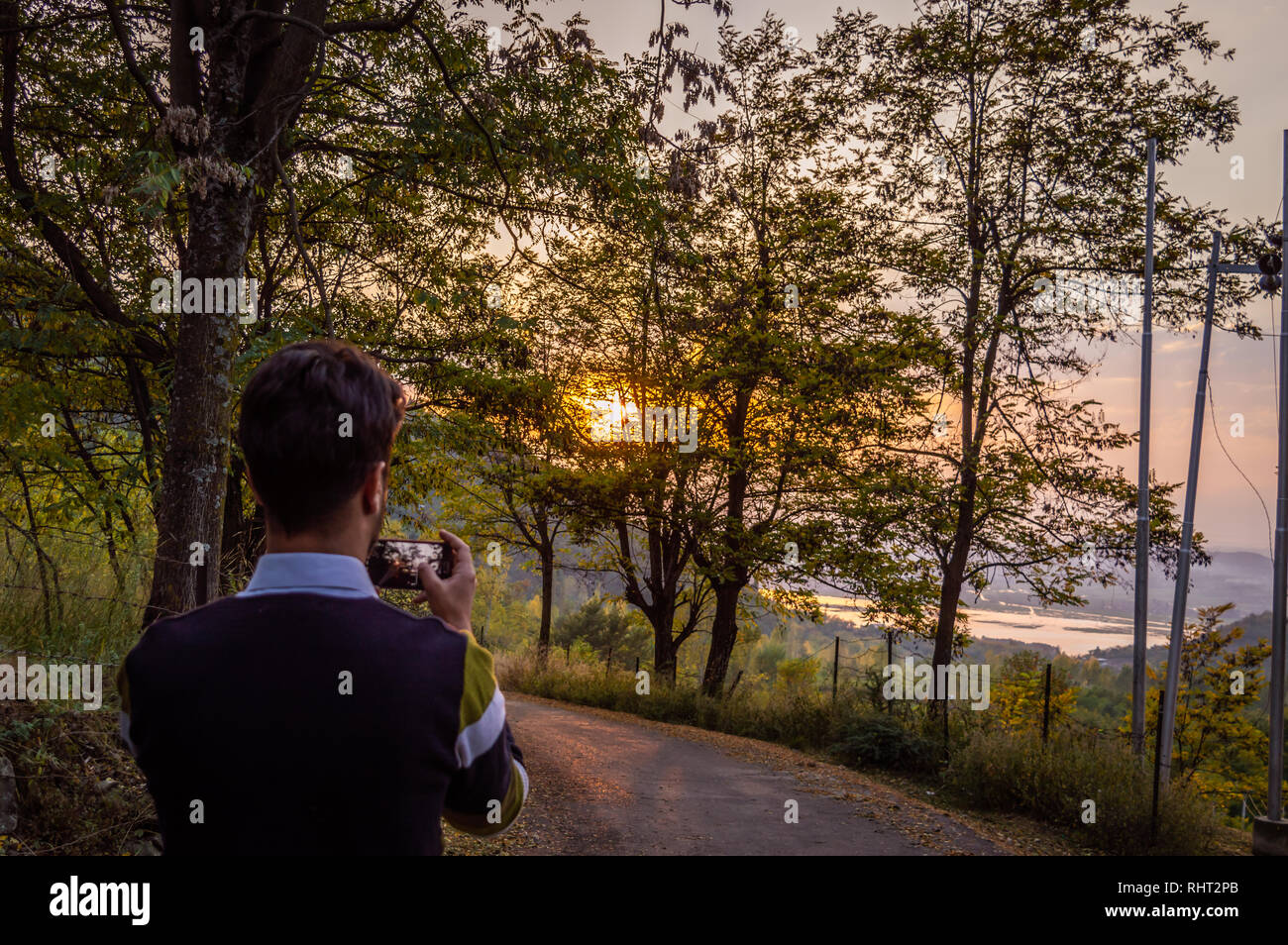 Eine Person mit seinem Smartphone das Foto eines Sonnenuntergangs in einem Wald zu nehmen Stockfoto