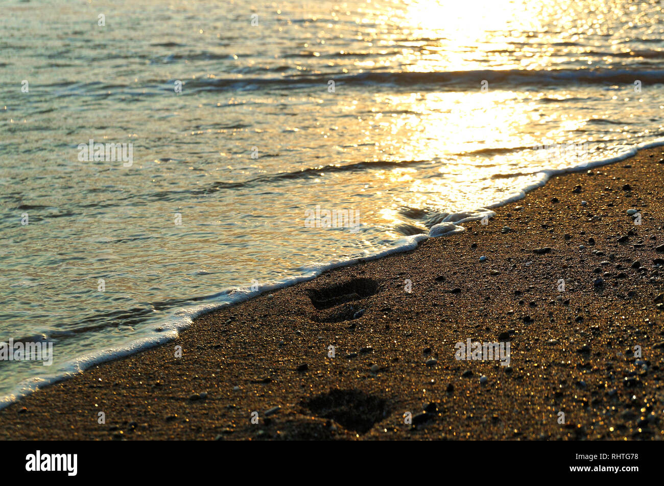 Vanishing Füßen Spuren aus Waschmaschine durch Wellen von Golden Beach Sand mit Reflexion der untergehenden Sonne in weichem Wasser Stockfoto