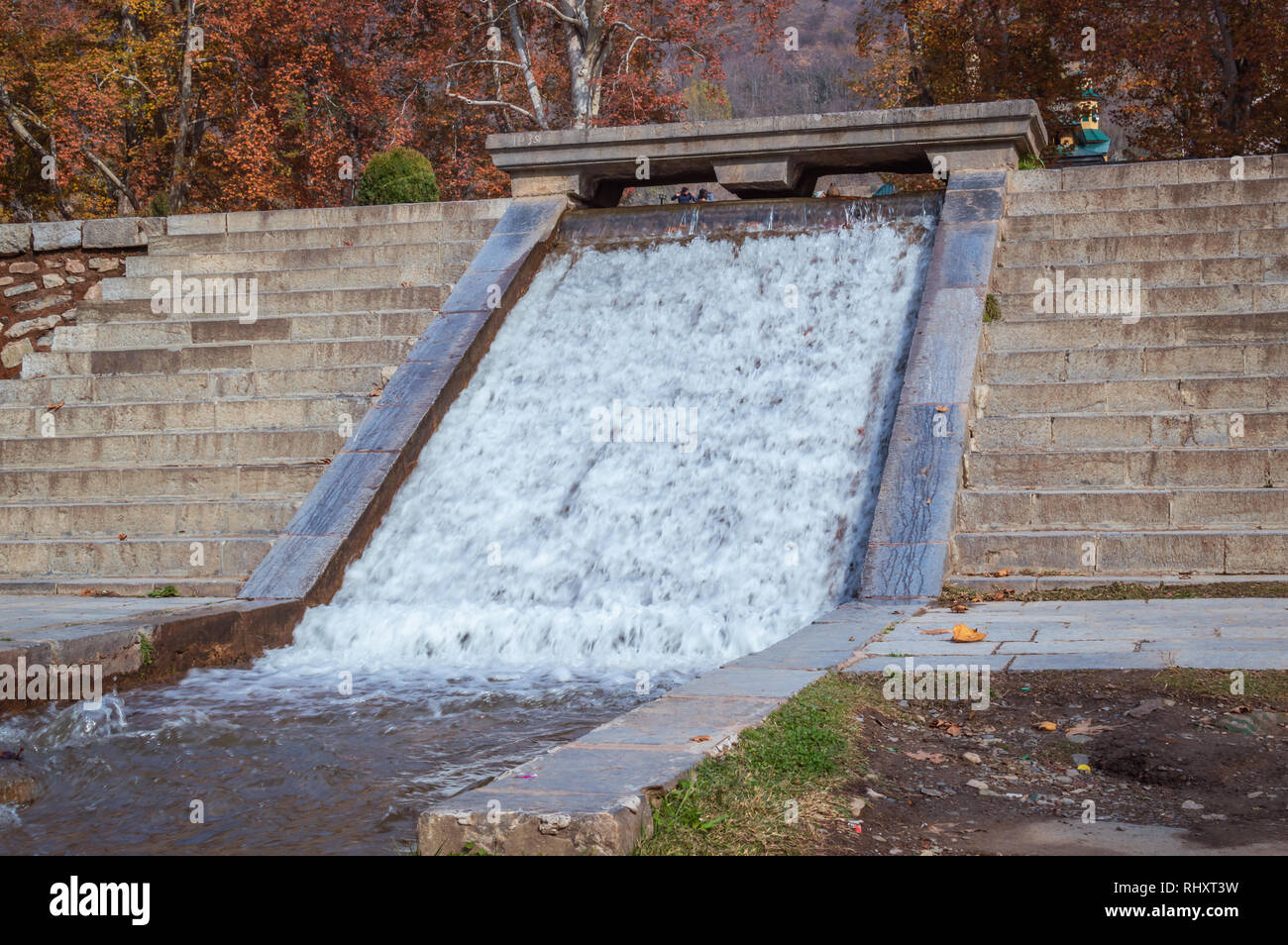 Ein künstlicher Wasserfall in einem öffentlichen Park. Bäume mit gelben Blätter im Herbst. Stockfoto