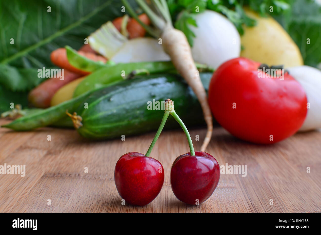 Bambus Schneidebrett voller Vitamine, ein paar frische, reife Kirschen im Vordergrund und viele verschiedene Art von Gemüse im Hintergrund Stockfoto