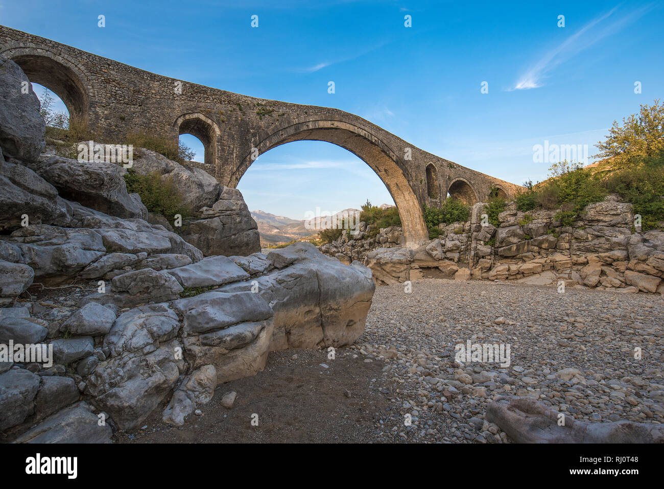 Die mesi Brücke (Ura e Mesit) in Mes, Albanien, in der Nähe von Shkodra. Ein alter Stein osmanische Brücke - die größte im Land. Trockenen Fluss und die Berge Stockfoto