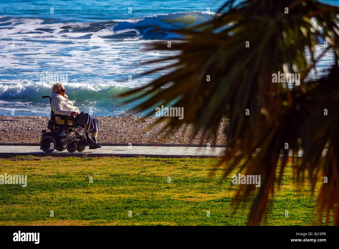 Ältere behinderte Dame im Rollstuhl auf Promenade und Meer mit Wellen in Oropesa del Mar Resort, Costa del Azahar, Provinz Castellon, Spanien, Oropesa Stockfoto