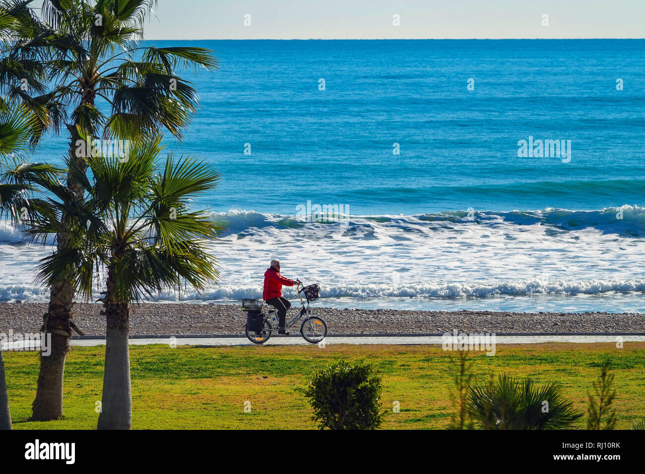 Ältere person Radfahren mit Elektrofahrrad, Promenade und Meer mit Wellen in Oropesa del Mar Resort, Costa del Azahar, Provinz Castellon, Spanien, Oropesa Stockfoto