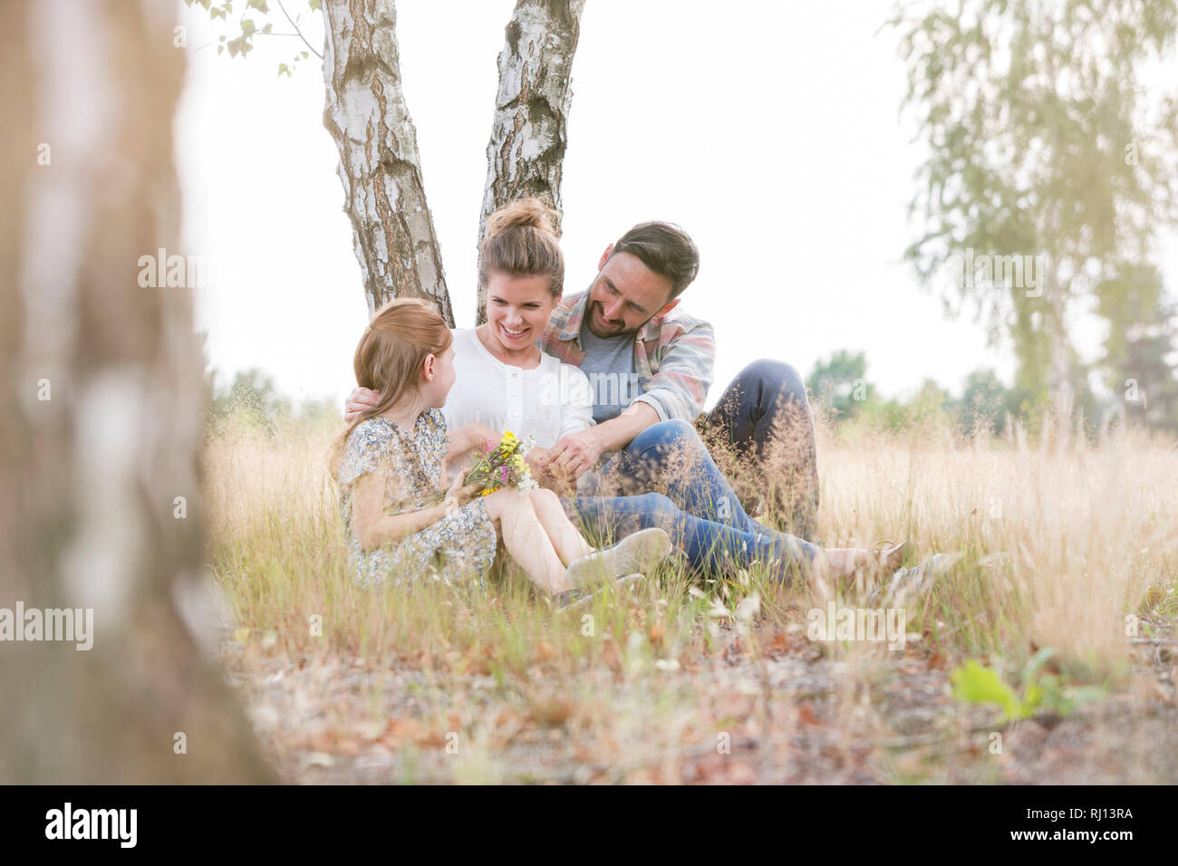 Glückliche Familie sitzen gegen Baum auf Feld bei Ackerland Stockfoto