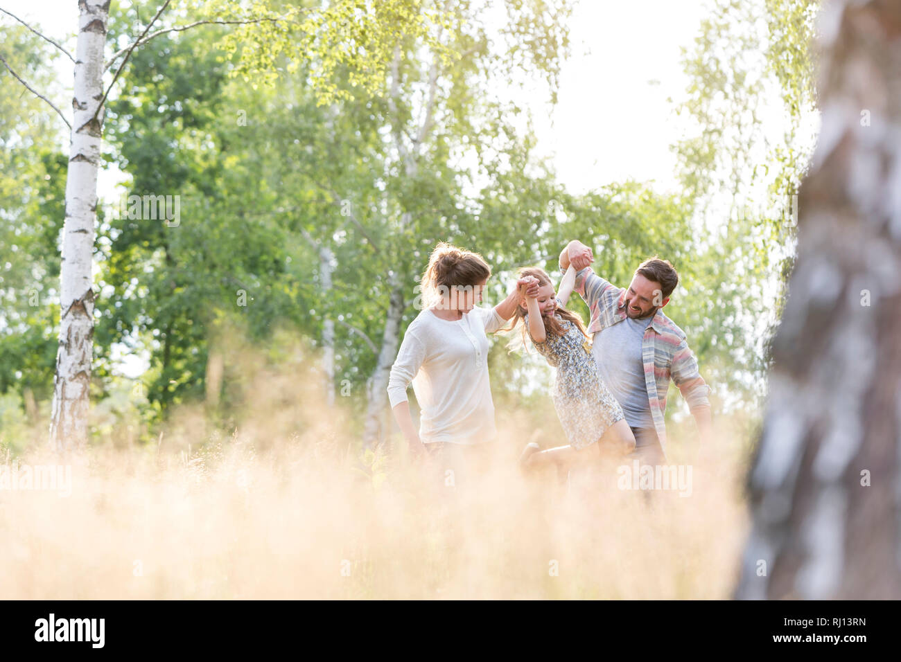 Glückliche Eltern spielt mit Tochter auf dem Feld gegen Bäume am Bauernhof Stockfoto