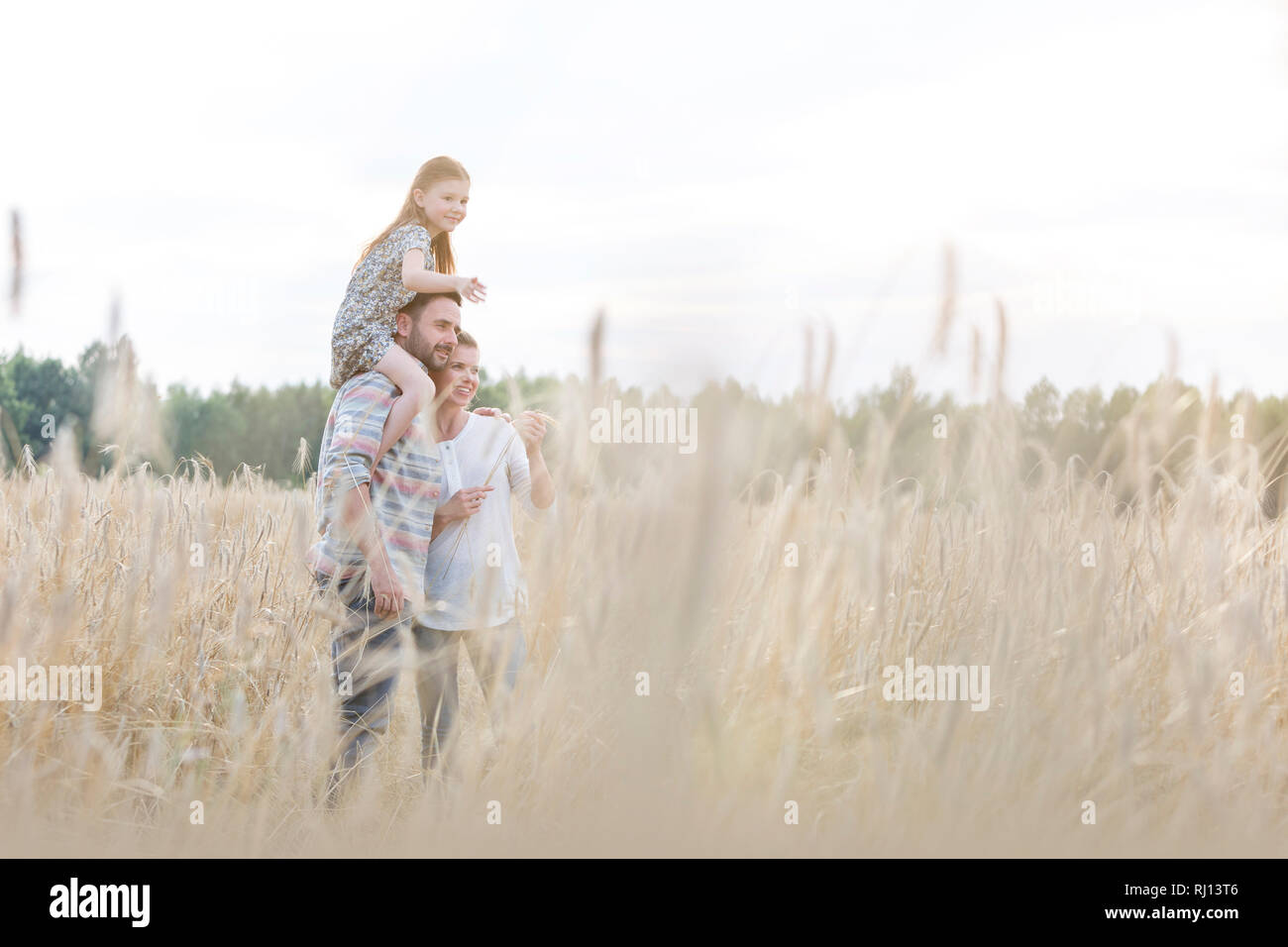 Vater mit Tochter auf Schultern mit Frau an Weizen Farm Stockfoto