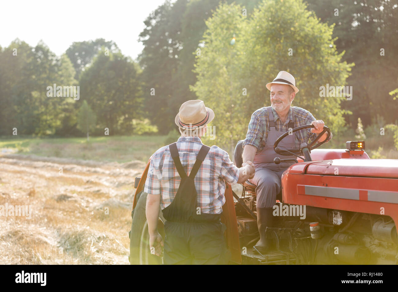 Landwirt Händeschütteln mit Kollegen sitzen auf Traktor am Bauernhof Stockfoto