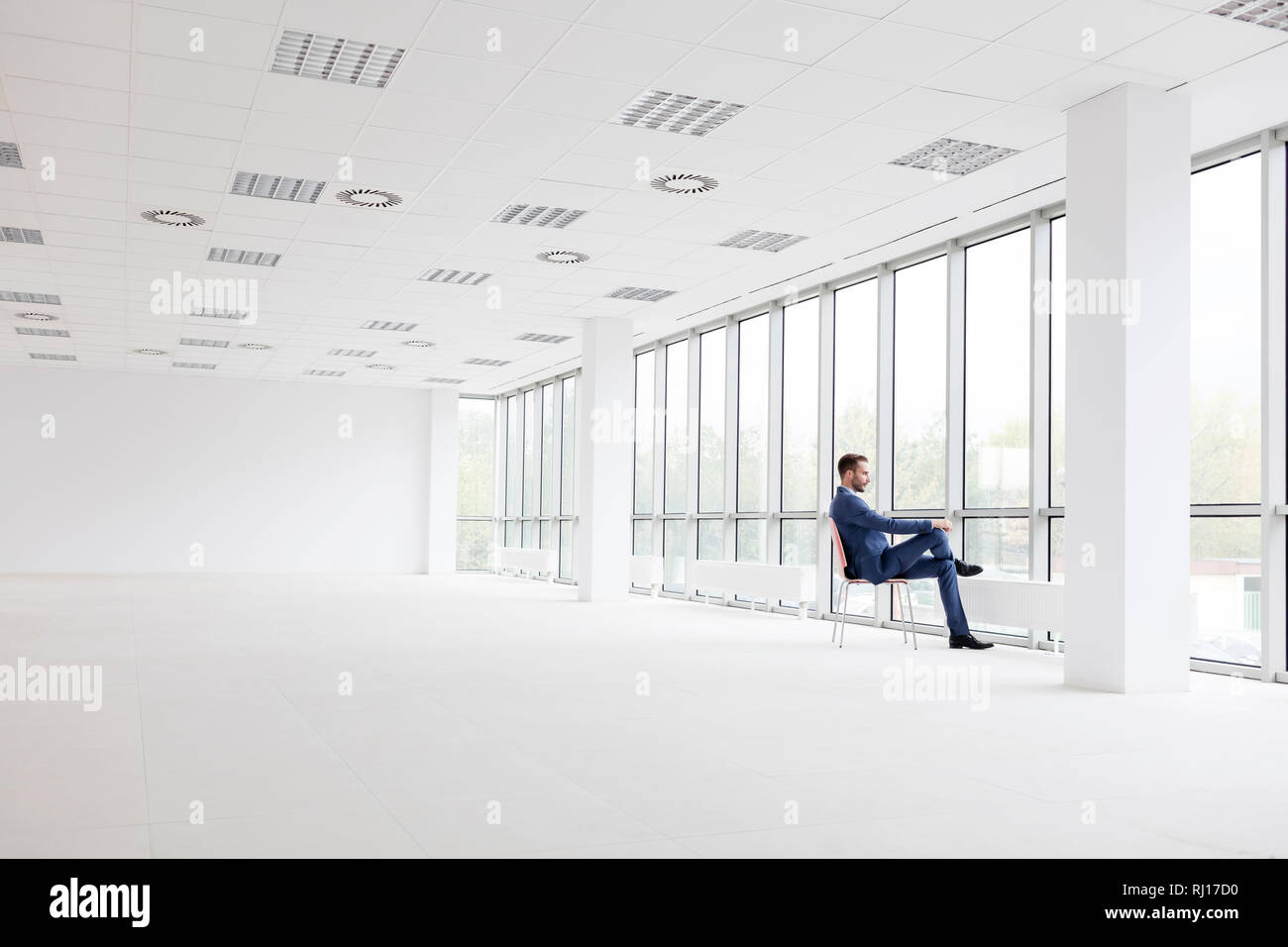 Die ganze Länge der nachdenkliche junge Unternehmer sitzen auf Stuhl, während Sie durch das Fenster an der neuen leeren Büro Stockfoto