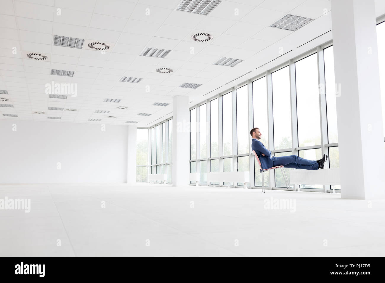 Die ganze Länge der nachdenkliche junge Unternehmer entspannt auf Stuhl, während Sie durch das Fenster an der neuen leeren Büro Stockfoto