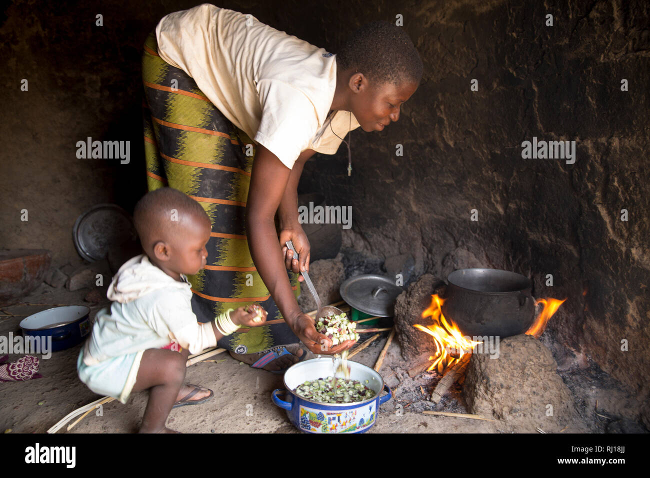 Samba Dorf, yako Provinz, Burkina Faso: Collette Guiguemde, 26, mit ihrem Baby Ornela göttlichen Zoundi, 18 Monate, Köche eine Mahlzeit für ihre Kinder und ihre Eltern-in-Gesetz mit der Okra sie gerade geerntet hat, und macht eine sorghum Brei oder Tao. Stockfoto