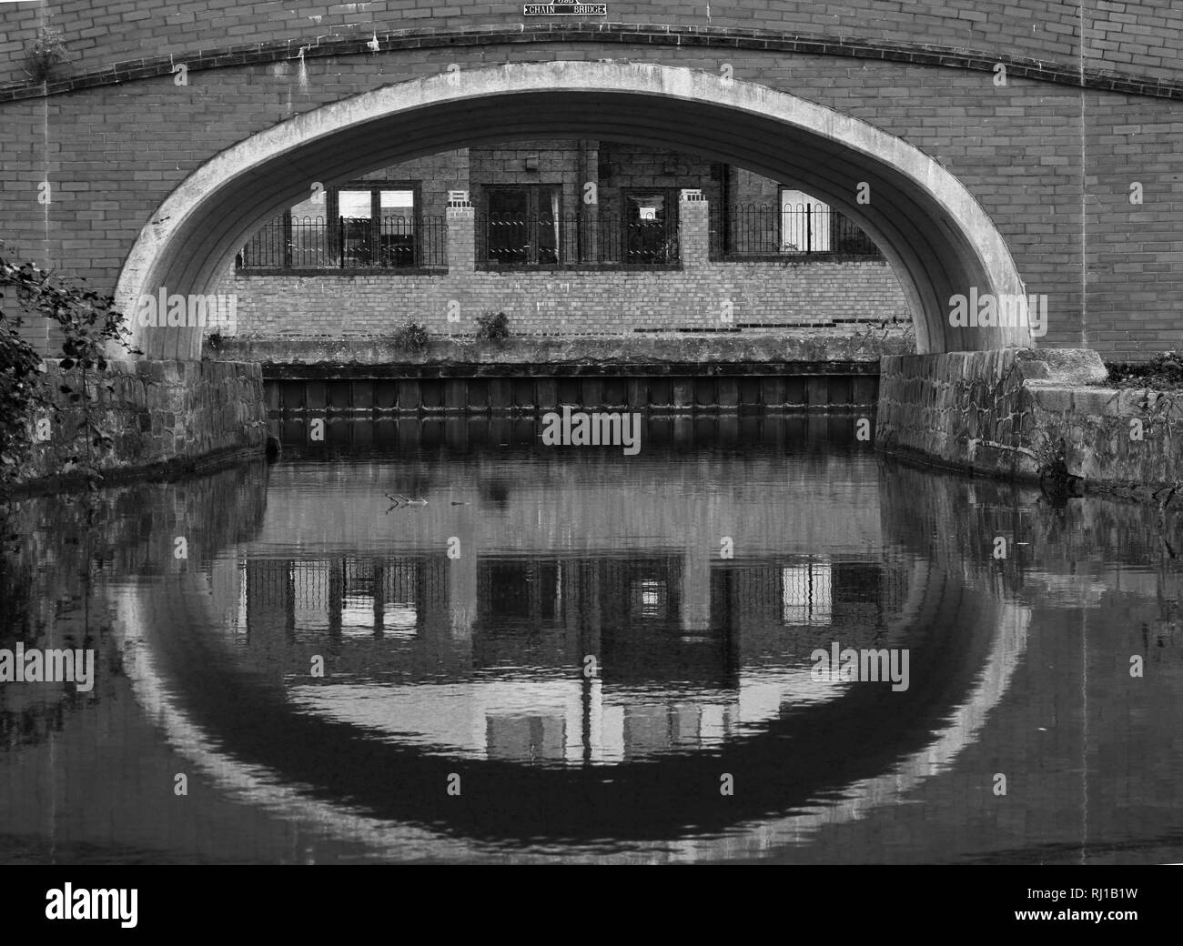 B&W gewölbte Brücke über den Kanal mit industriellen Gebäuden Stockfoto