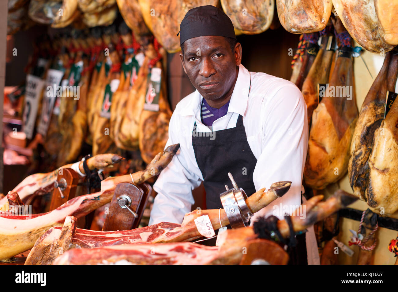 Portrait von erfahrenen Afrikaner Metzger auf dem Hintergrund der Rack mit hängenden verschiedene Jamon im Shop Stockfoto