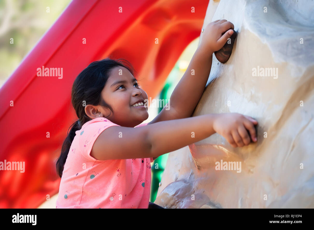 Indisches Mädchen mit einem Lächeln auf ihrem Gesicht hält sich an einer Kletterwand und freuen uns auf die physische Herausforderung. Stockfoto