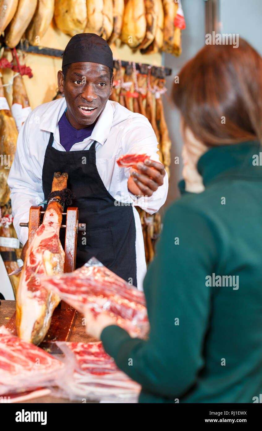 Heiter erfolgreiche Metzger mit köstlichen spanischen Schinken zu den weiblichen Klienten in Fleisch Delikatessengeschäft Stockfoto