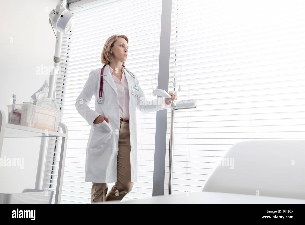Nachdenklich reife Arzt steht die Messskala, während Sie durch das Fenster am Krankenhaus Stockfoto
